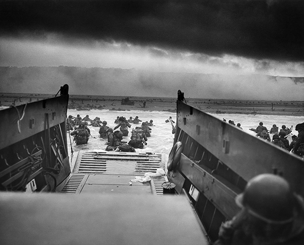 “Un LCVP (Landing Craft, Vehicle, Personnel) della Guardia Costiera degli Stati Uniti – portato sul posto dalla USS Samuel Chase – sbarca le truppe della 1ª Divisione di Fanteria (il Grande Uno Rosso). I soldati americani si scontrano con la 352ª Divisione tedesca, appena costituita. Durante lo sbarco iniziale la Compagnia E ha perso due terzi dei suoi effettivi”. 6 giugno 1944. Spiaggia di Omaha, Normandia, Francia. Fotografo: sconosciuto o non fornito. Per gentile concessione degli U.S. National Archives